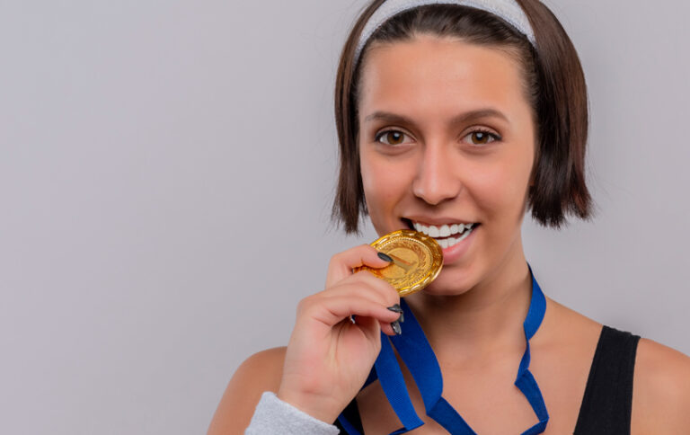 Joven con medalla deportiva sonriendo relación entre el deporte y la salud bucodental
