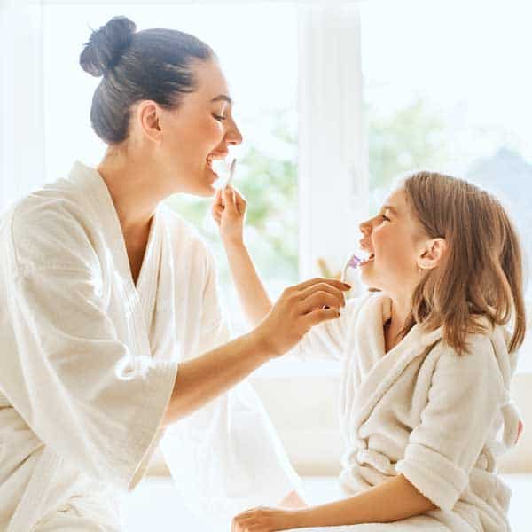 Madre e hija cepillándose los dientes juntas hábitos de higiene dental en familia