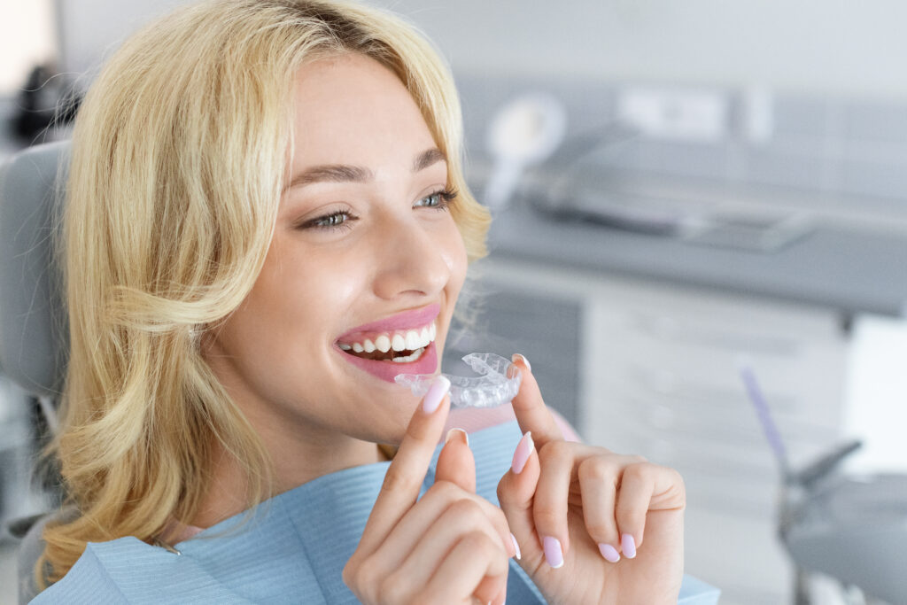 Mujer joven sonriendo y sosteniendo un alineador invisible de ortodoncia Invisalign