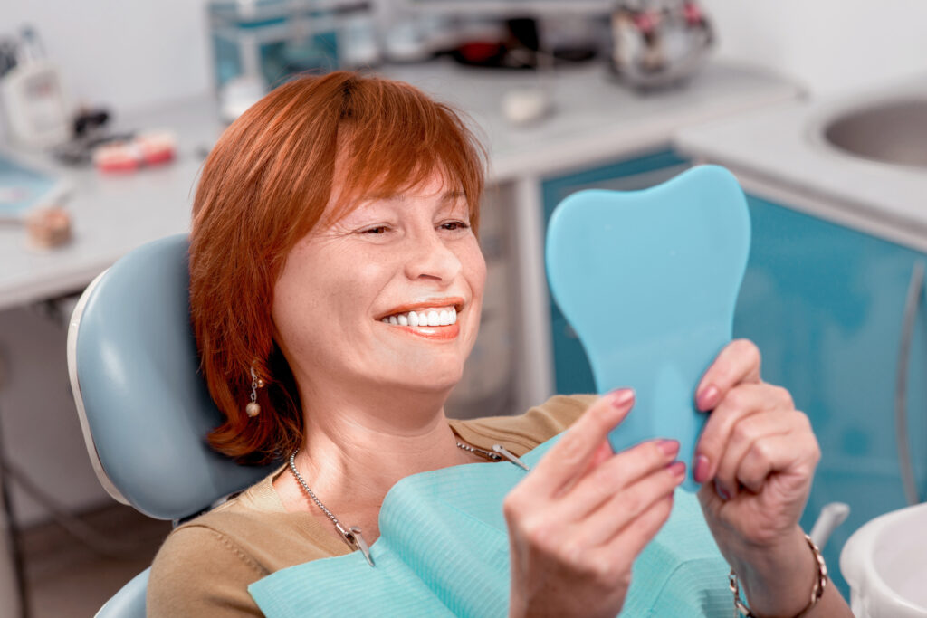 Mujer pelirroja revisando su sonrisa con un espejo en sillón dental