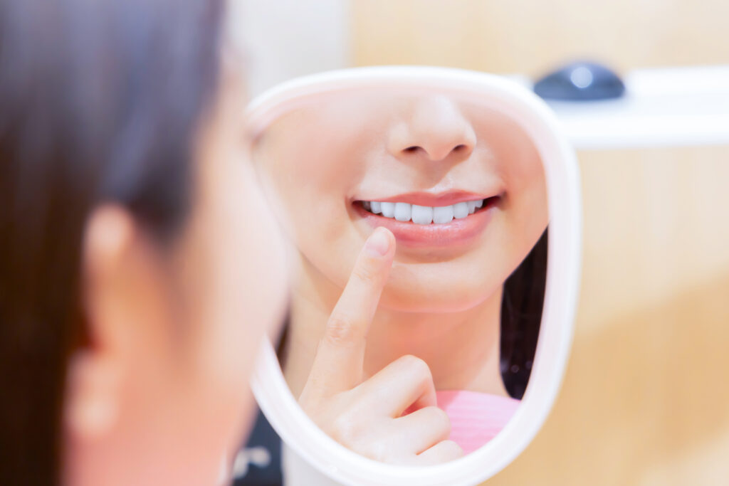 Mujer revisando su sonrisa en espejo de mano